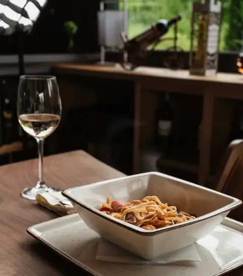 Linguini dhe verë e bardhë pranë dritares me gjelbërim