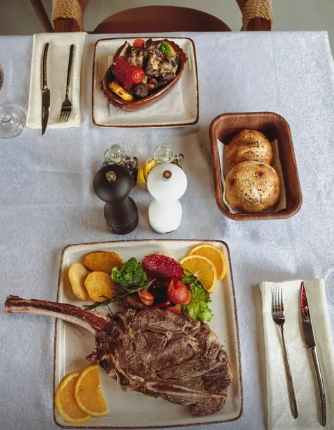 Tavolinë e shtruar me tomahawk, tavë dhe bukë të ngrohtë